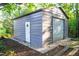 A metal shed with a garage door and entry door in a wooded backyard at 1023 Laura Johnson Rd, Pittsboro, NC 27312
