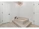 Stylish soaking tub with travertine floors, black faucet, and modern light fixture at 1412 Amberton Ct, Raleigh, NC 27615