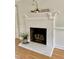 A close-up view of a living room fireplace with a white painted brick surround, wooden mantel, and hardwood floors at 1002 Springmill Ct, Apex, NC 27502