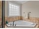 Corner bathtub surrounded by beige tiling with large window providing natural light at 2053 Monthaven Dr, Wake Forest, NC 27587