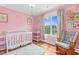 A bright and airy pink-themed room with a crib, rocking chair, and large window at 11 Glen Valley Ct, Angier, NC 27501