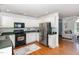 Spacious kitchen with white cabinets, black appliances, stainless fridge, and hardwood floors leading into the living room at 9404 Dawnshire Rd, Raleigh, NC 27615