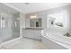 Bright bathroom features a soaking tub, a glass shower, white cabinets, gray countertops, and marble floors at 1429 Wragby Ln, Apex, NC 27502