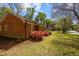 Side exterior of brick home featuring a well-maintained lawn, mature trees, and flowering bushes at 3126 Truitt Dr, Burlington, NC 27215