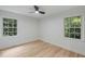 This bright bedroom features wood-look floors, a modern ceiling fan, and two windows with views of lush greenery at 6421 Arrington Rd, Raleigh, NC 27607