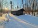 Modern black house featuring snow covered ground, illuminated by the sun, surrounded by bare trees at 665 Lonach Ln, Roxboro, NC 27574