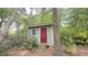 Small shed with a red door and window, nestled among trees and greenery, providing extra storage space at 7312 Ray Rd, Raleigh, NC 27613