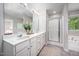 Bright bathroom featuring double vanity, walk-in shower, neutral walls, and window views of the lush scenery at 15 White Spruce Ct, Durham, NC 27703