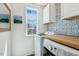 Bright laundry room with stackable washer and dryer, white cabinets, and decorative blue-tiled backsplash at 5172 Copain Cove, Fuquay Varina, NC 27526
