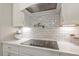 Modern kitchen with white cabinets, a tile backsplash, and a sleek black stovetop at 101 Jewell Farm Lane, Holly Springs, NC 27540
