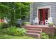 Inviting brick porch with white Adirondack chairs and a red door, surrounded by lush landscaping at 1603 Hermitage Ct, Durham, NC 27707