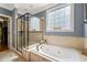 Bright bathroom boasts a glass shower, soaking tub, neutral tile surround, and picture window at 19002 Stone Brk, Chapel Hill, NC 27517