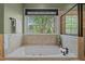 Relaxing soaking tub with tile surround and a large window overlooking the backyard at 321 Nortwick Rd, Rolesville, NC 27571