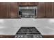 Close-up of kitchen features a gas range, microwave, and white subway tile backsplash beneath dark wood cabinets at 615 Prides Crsg Xing, Rolesville, NC 27571