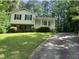 Two-story home with yellow siding, brick foundation, covered front porch, lush greenery, and a long driveway at 7412 Barberry Ct, Raleigh, NC 27615