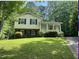 Two-story home with yellow siding, brick foundation, covered front porch, and manicured lawn surrounded by lush greenery at 7412 Barberry Ct, Raleigh, NC 27615