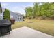 Landscaped backyard featuring mature trees, a lush green lawn, a concrete patio, and home's blue siding at 10 Currituck Ln, Durham, NC 27703