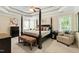 This large main bedroom features a tray ceiling, four-poster bed, bench, and an armchair at 10113 San Remo Pl, Wake Forest, NC 27587