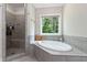Bright bathroom features a large soaking tub and a tiled shower, with a window overlooking a wooded backyard at 120 Wood Lake Dr, Fuquay Varina, NC 27526
