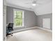 Bright, empty bedroom with a large window, soft carpet, and an attic door at 121 Cobblepoint Way, Holly Springs, NC 27540