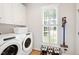 Bright laundry room with tile floors, washer, dryer, storage, and natural light from shuttered window at 4900 Old Millcrest Ct, Raleigh, NC 27609