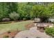 Lush backyard with manicured lawn, mature trees, and a stone patio with outdoor seating at 112 Aspenridge Dr, Holly Springs, NC 27540