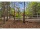 Wooded backyard featuring a white fence, mature trees, and a glimpse of the brick home and patio at 2925 Ericka Dr, Hillsborough, NC 27278