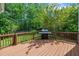 Back deck with wood railing and a grill, surrounded by lush green trees in a private backyard at 1198 Shining Water Ln, Creedmoor, NC 27522