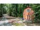 Rustic orange outbuilding with white doors nestled in lush greenery and a gravel driveway at 82 Deercorn Path, Moncure, NC 27559
