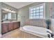 Elegant bathroom featuring soaking tub, wooden cabinets, granite countertops, tiled floors, and window at 628 Carolina Crossings Dr, Apex, NC 27523