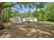 A spacious yard surrounded by lush trees, with a view of the back exterior of the home and the outbuildings at 701 Oakwood St, Mebane, NC 27302