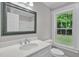 Bright bathroom featuring a large mirror and vanity, a white commode, and a window overlooking the lush outdoors at 701 Oakwood St, Mebane, NC 27302