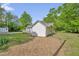 Shows the exterior of the house on the side with green grass and mulch, and an outbuilding in the background at 701 Oakwood St, Mebane, NC 27302