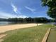 Sandy beach volleyball court surrounded by green grass and tall trees under a clear blue sky with wispy clouds at 118 Chanute Cir, Louisburg, NC 27549