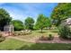 Picturesque backyard featuring a fire pit with Adirondack chairs, colorful flower beds, mature trees, and a garden shed at 220 Lakecroft Pl, Fuquay Varina, NC 27526