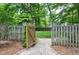 Backyard with a wooden gate and a gravel path leading to a lush green lawn surrounded by trees at 5112 Wolcott Ct, Fuquay Varina, NC 27526