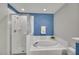 Bright bathroom featuring a soaking tub, glass enclosed shower, and blue accent wall at 5547 Sea Daisy Dr, Raleigh, NC 27606