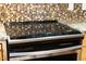 Close up of a glass top electric stove top with granite countertops and mosaic backsplash at 105 Parkmount Cir, Cary, NC 27519