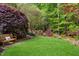 Serene backyard featuring a bench, lush green lawn, mature trees, and colorful landscaping at 754 Olde Thompson Creek Ct Rd, Apex, NC 27523