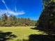 Open field with lush green grass bordering a serene wooded area with mature trees under a blue sky at 79 Mildred Dr, Broadway, NC 27505