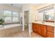 Well-lit bathroom with a soaking tub, wood cabinets, tile floors, and a large mirror at 1003 Red Sunset Dr, Apex, NC 27502