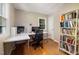 Well-lit home office with hardwood floors, a white desk setup, and a bookcase filled with books at 1506 Ephesus Church Rd, Chapel Hill, NC 27517