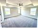 Spacious primary bedroom with neutral carpeting, tray ceiling with fan, and three windows for natural light at 356 Bishop Ln, Sanford, NC 27330
