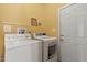 Bright laundry room featuring yellow walls, appliances, a white door, and built-in shelving at 6 Chelan Ct, Durham, NC 27713