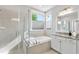 Bright bathroom with a tub under a window, walk-in shower, and white vanity with a granite countertop at 707 Sasser St, Raleigh, NC 27604
