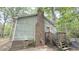 View of the home's side, featuring a brick chimney, green siding, and a wooden staircase leading to a red-trimmed back door at 7312 Ray Rd, Raleigh, NC 27613