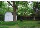 A white shed sits within a shady backyard with mature trees and a wooden fence at 1013 Green St, Durham, NC 27701