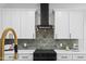 Close-up of modern kitchen features black range hood, granite backsplash, and white cabinets at 107 Seminole Dr, Louisburg, NC 27549