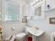 Bright bathroom featuring a pedestal sink, toilet, window with blinds, and storage cabinet at 224 E Park Dr, Raleigh, NC 27605
