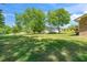 Lush backyard featuring mature trees, a vast lawn, and distant views of the charming outbuildings and brick home at 4418 Carpenter Pond Rd, Durham, NC 27703